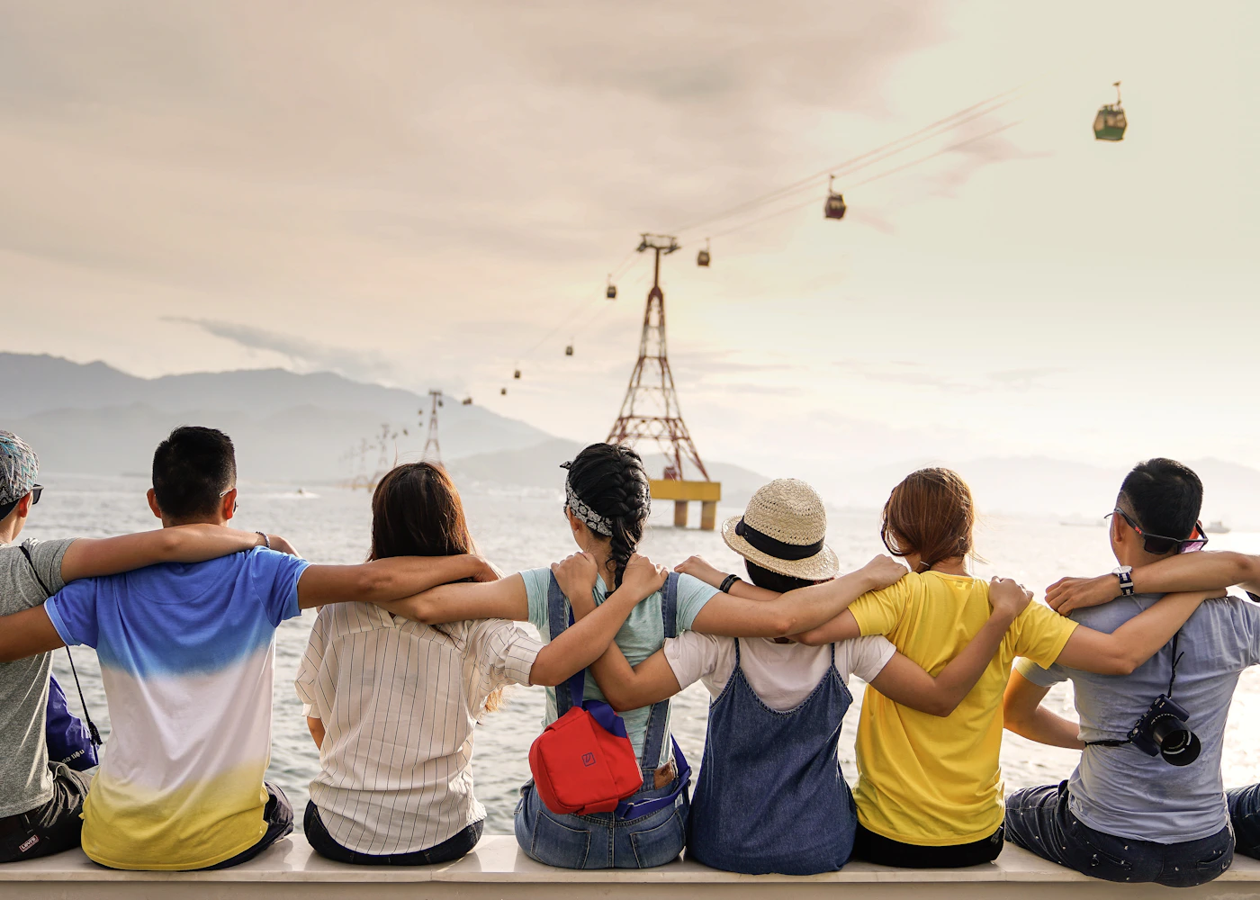 Friends with their arms around each other overlooking a sunny seaside bay